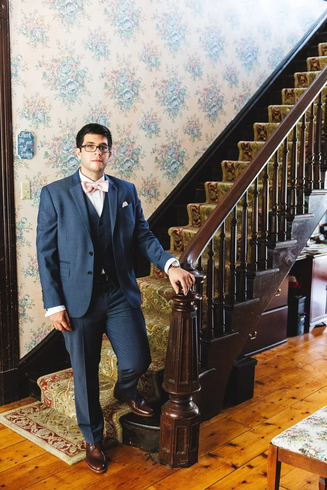 Groom in a blue three-piece suit beside a wooden staircase