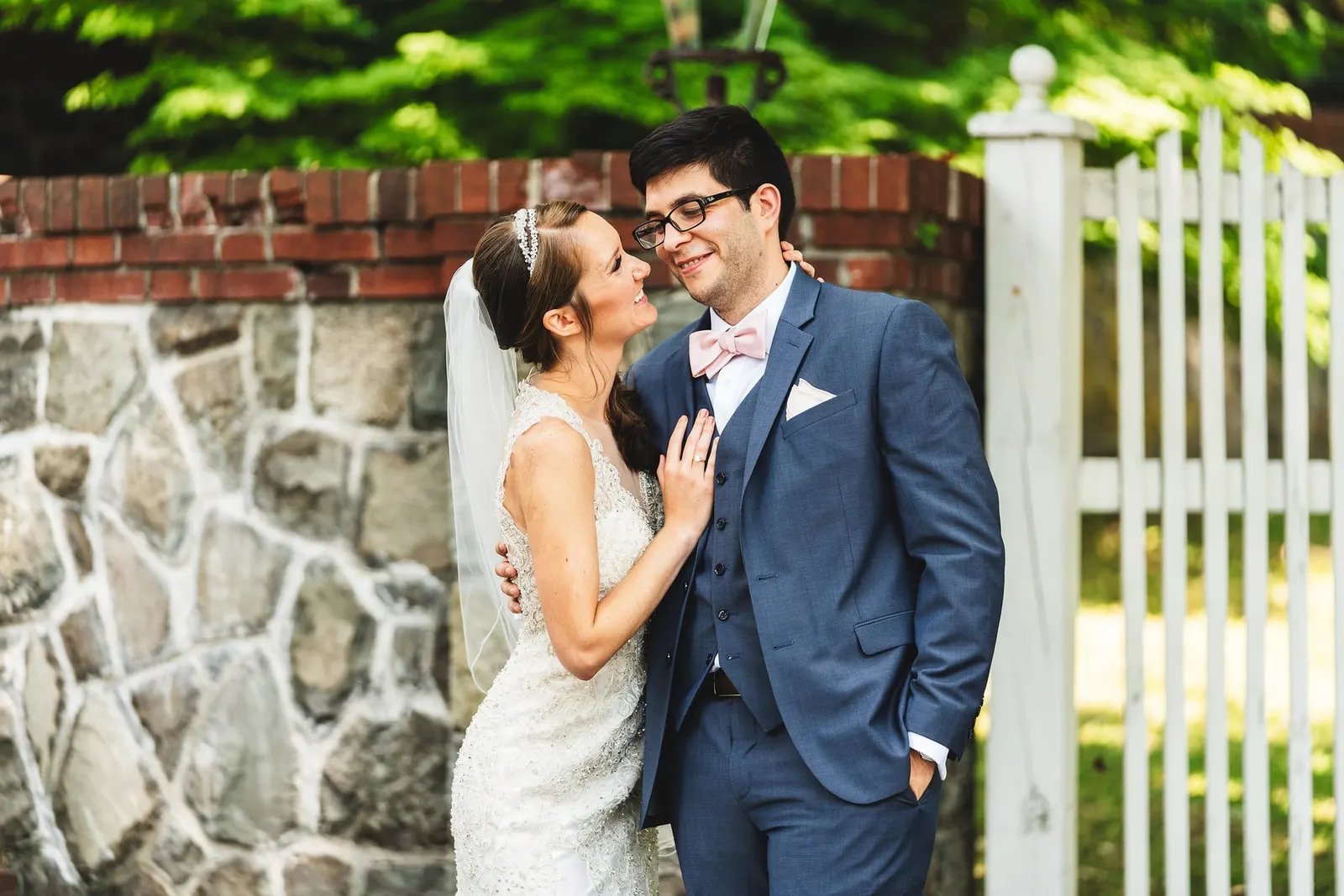 Bride and groom laughing together by a white picket fence