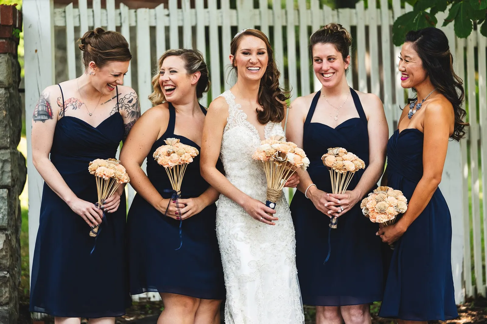 Bride laughing with her bridesmaids, all holding peach bouquets