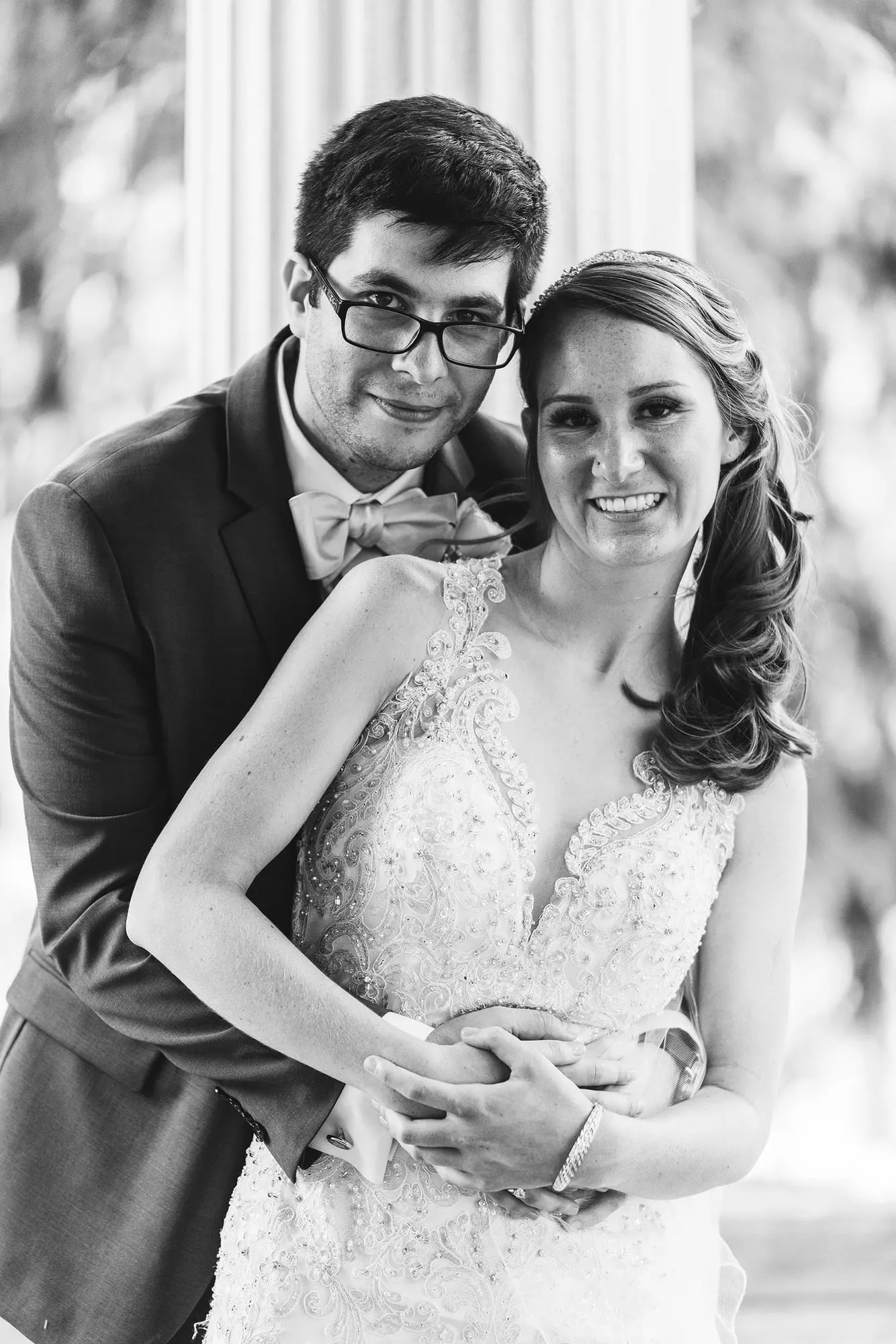 Black and white portrait of the groom hugging the bride from behind