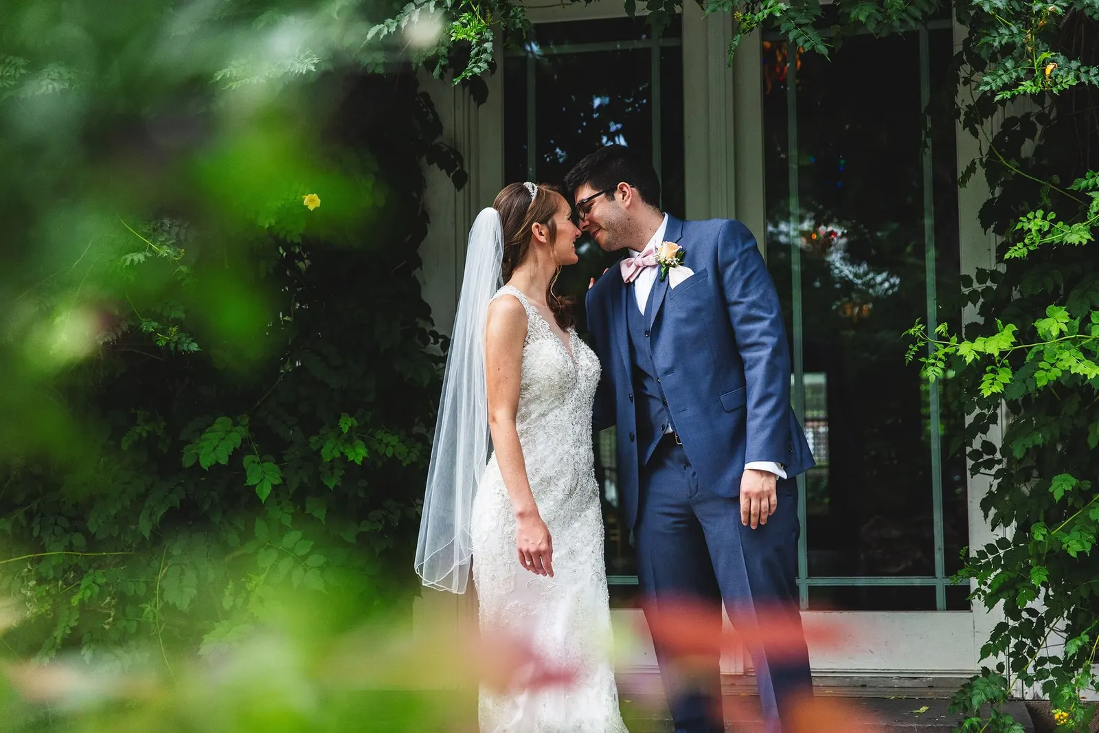 Bride and groom sharing a kiss framed by greenery