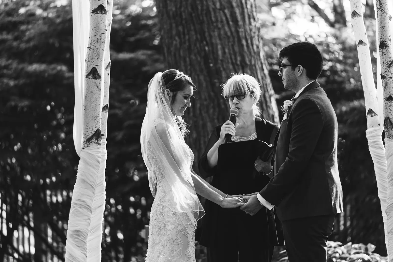 Black and white photo of the couple holding hands as the officiant speaks