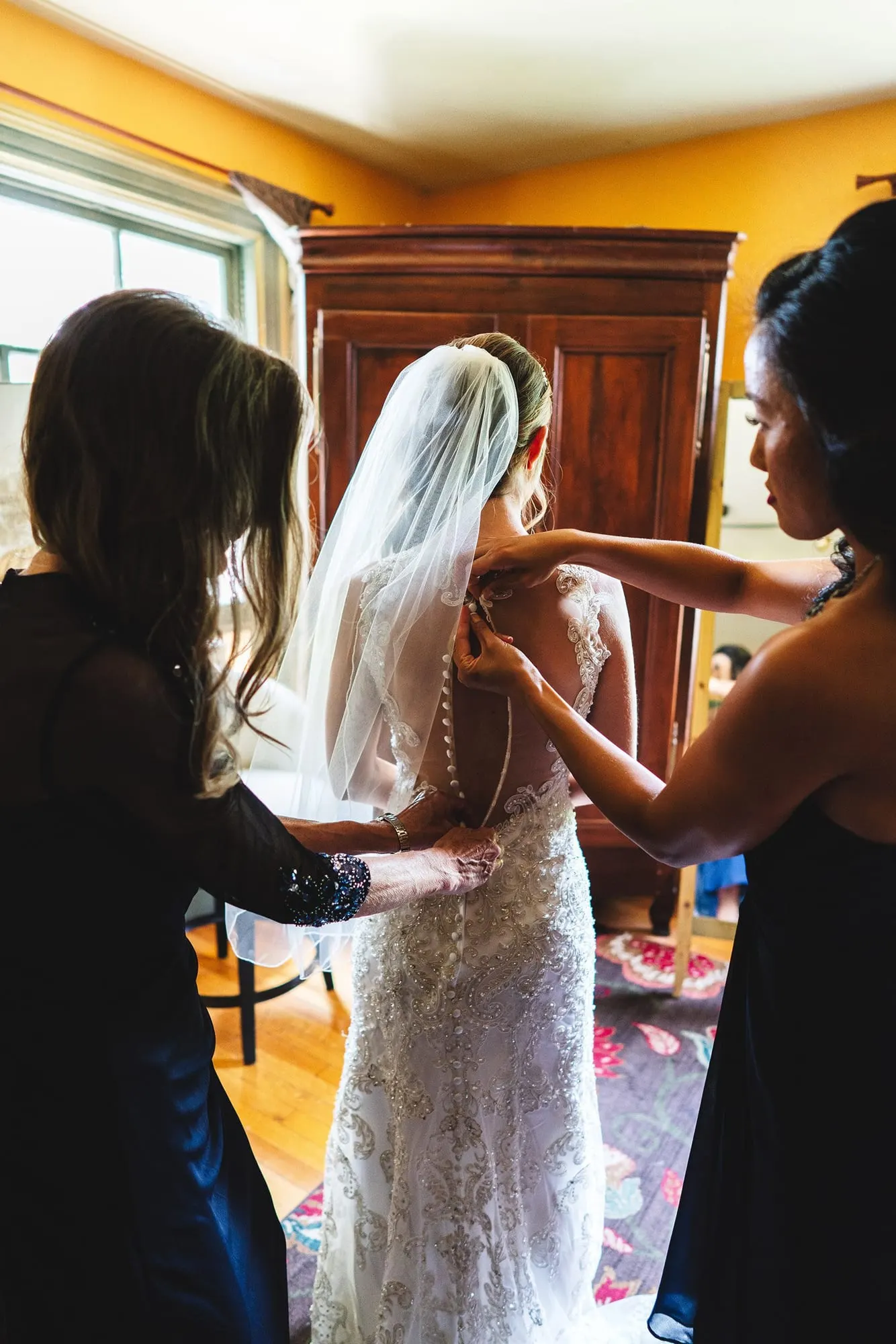 Bridesmaids buttoning the back of the bride's gown