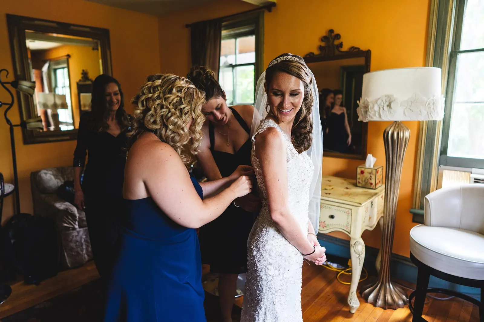 Bridesmaids helping the bride into her gown in a sunny yellow room