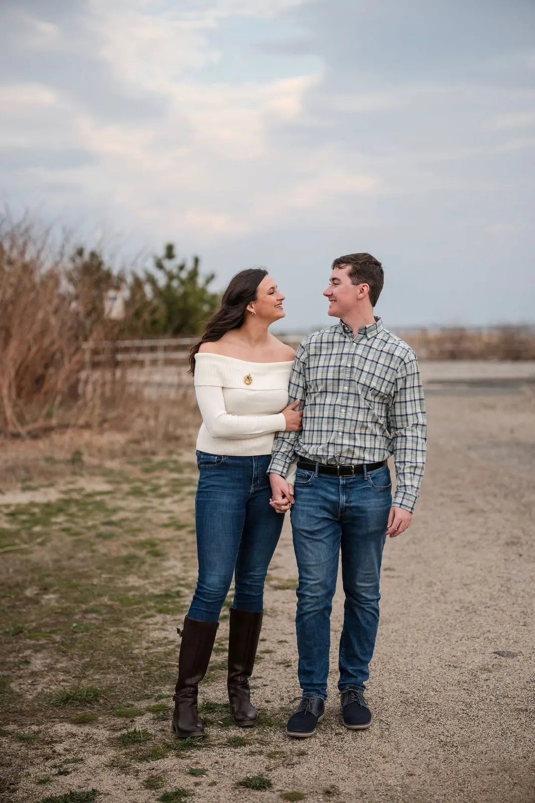 Engaged couple walking hand in hand on a path through beach grass near Wesley Lake