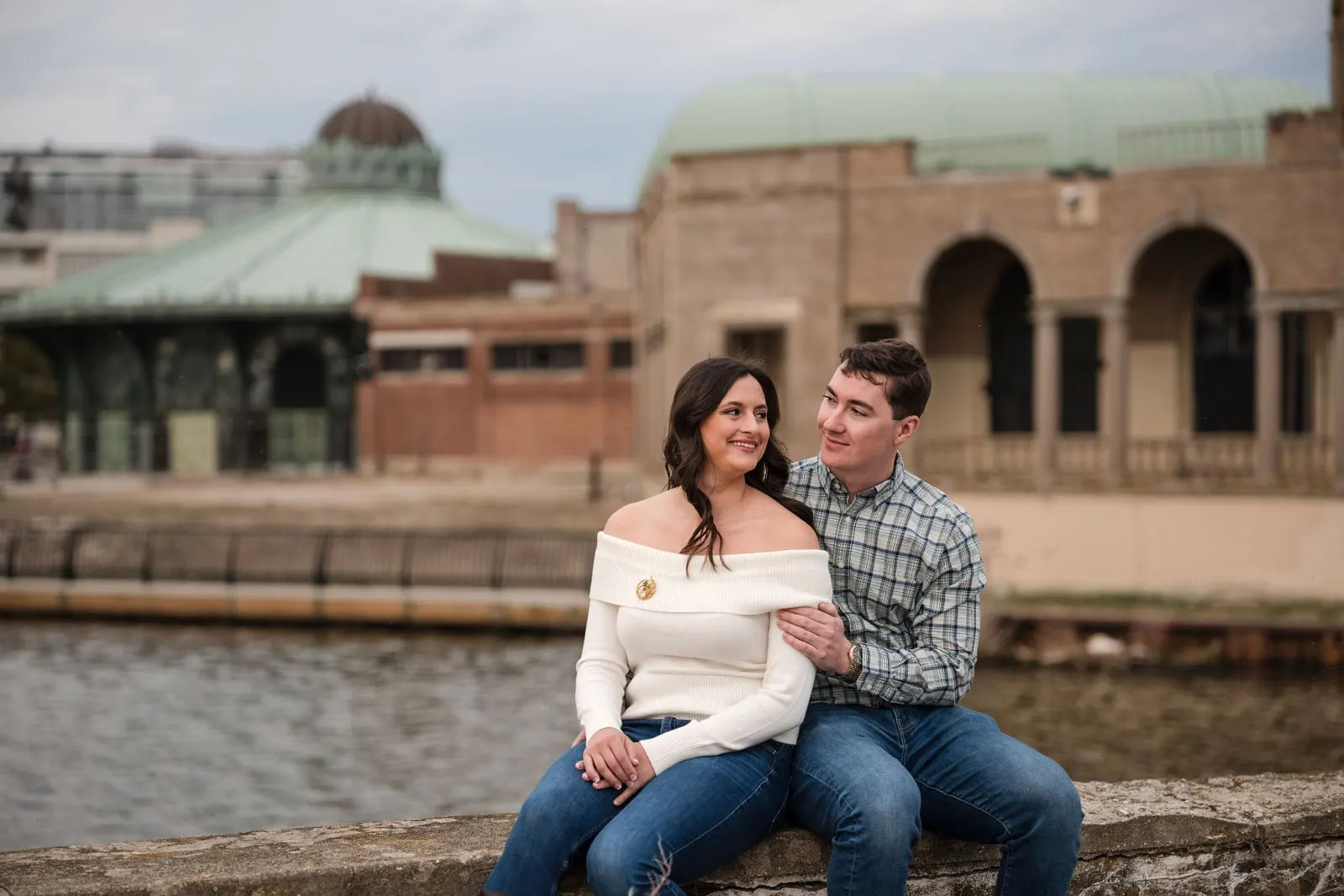 Couple sitting on a wall by Wesley Lake with the Asbury Park Casino and carousel house behind them