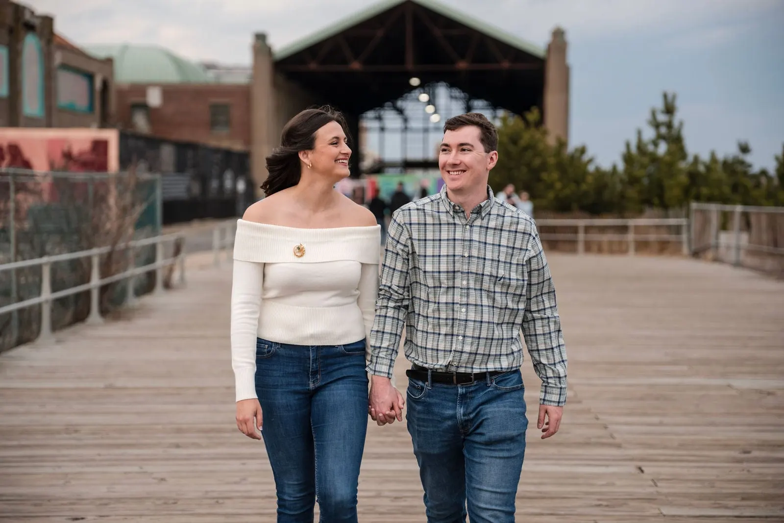 Engaged couple walking on the boardwalk in front of the steel arches of the Asbury Park Casino