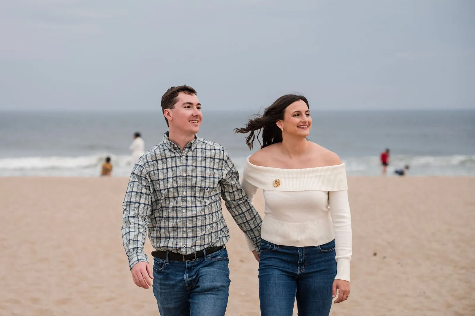 Engaged couple walking along the beach with the ocean behind them