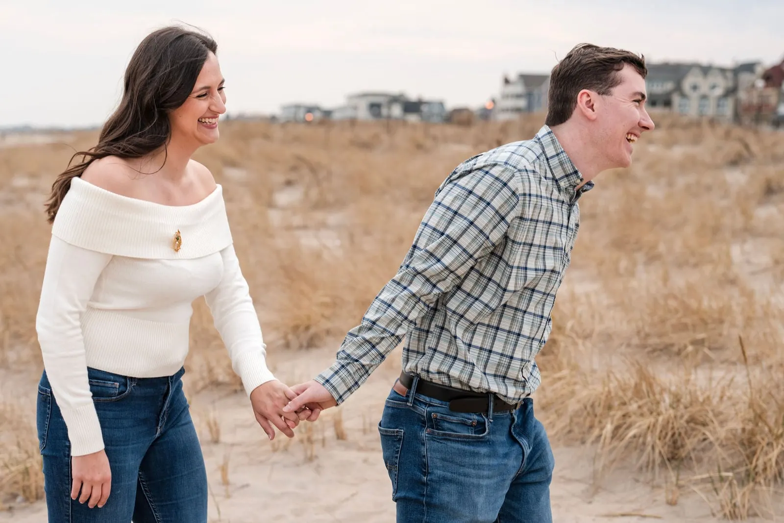 Engaged couple laughing as they walk through the dunes