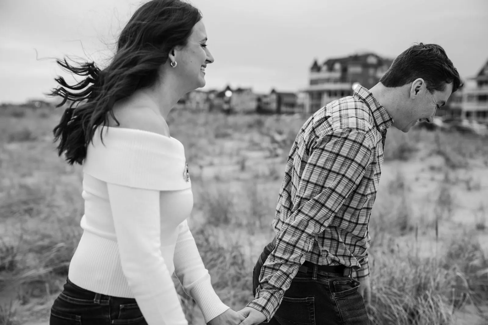 Black and white photo of the bride-to-be's hair blowing in the wind as the couple walks through the dunes