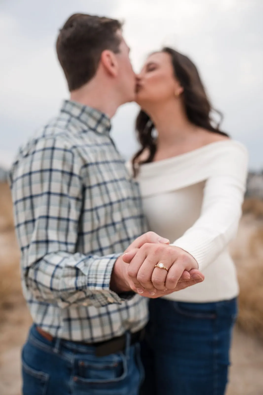 Couple kissing with their hands and engagement ring in focus