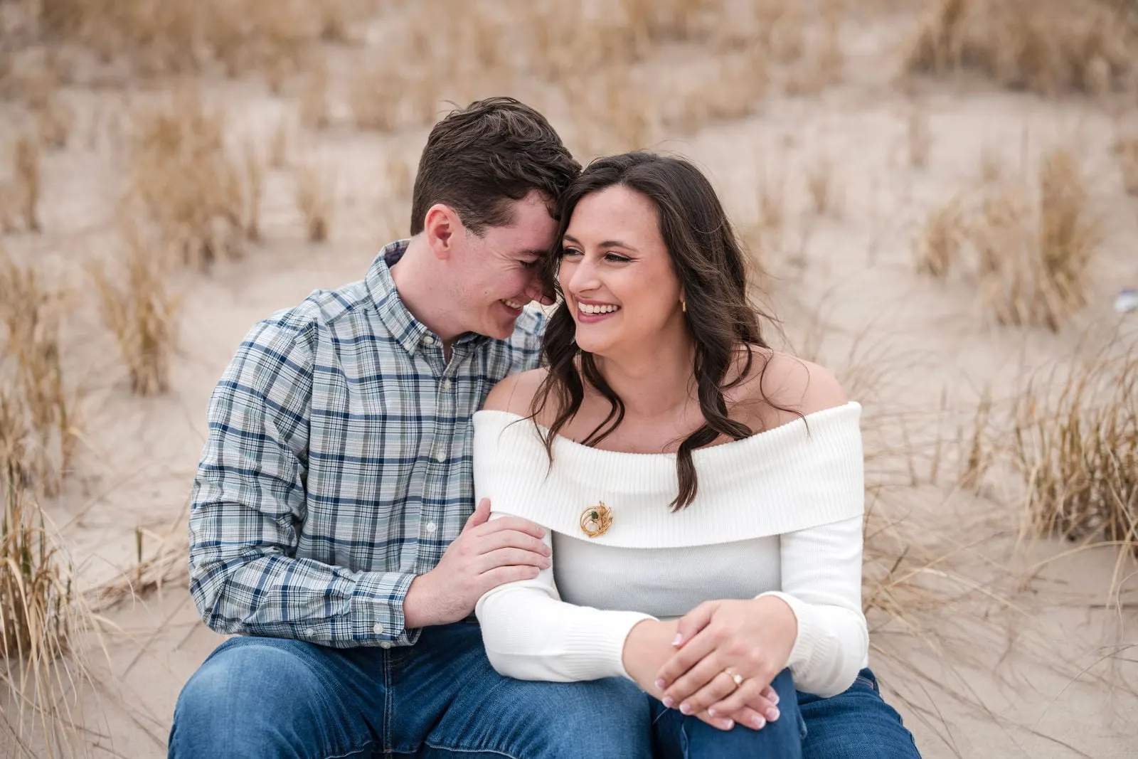Engaged couple sitting together in the golden dune grass on the beach in Asbury Park, New Jersey