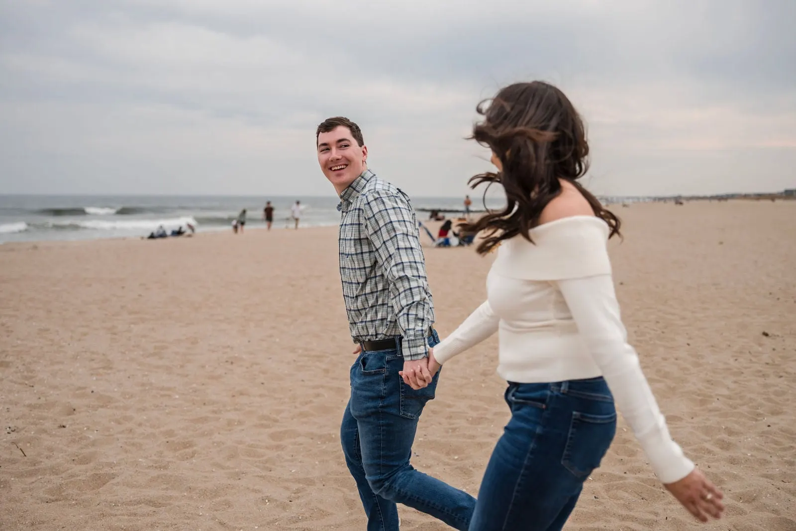 Engaged couple laughing as they walk across the beach in the wind