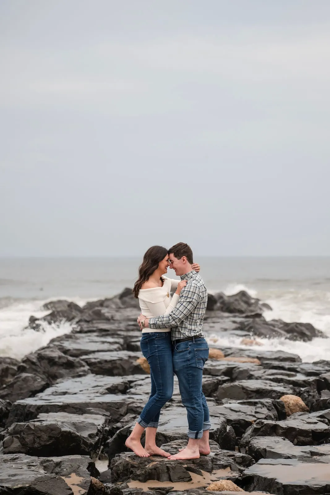 Barefoot couple touching foreheads on a rock jetty in Asbury Park