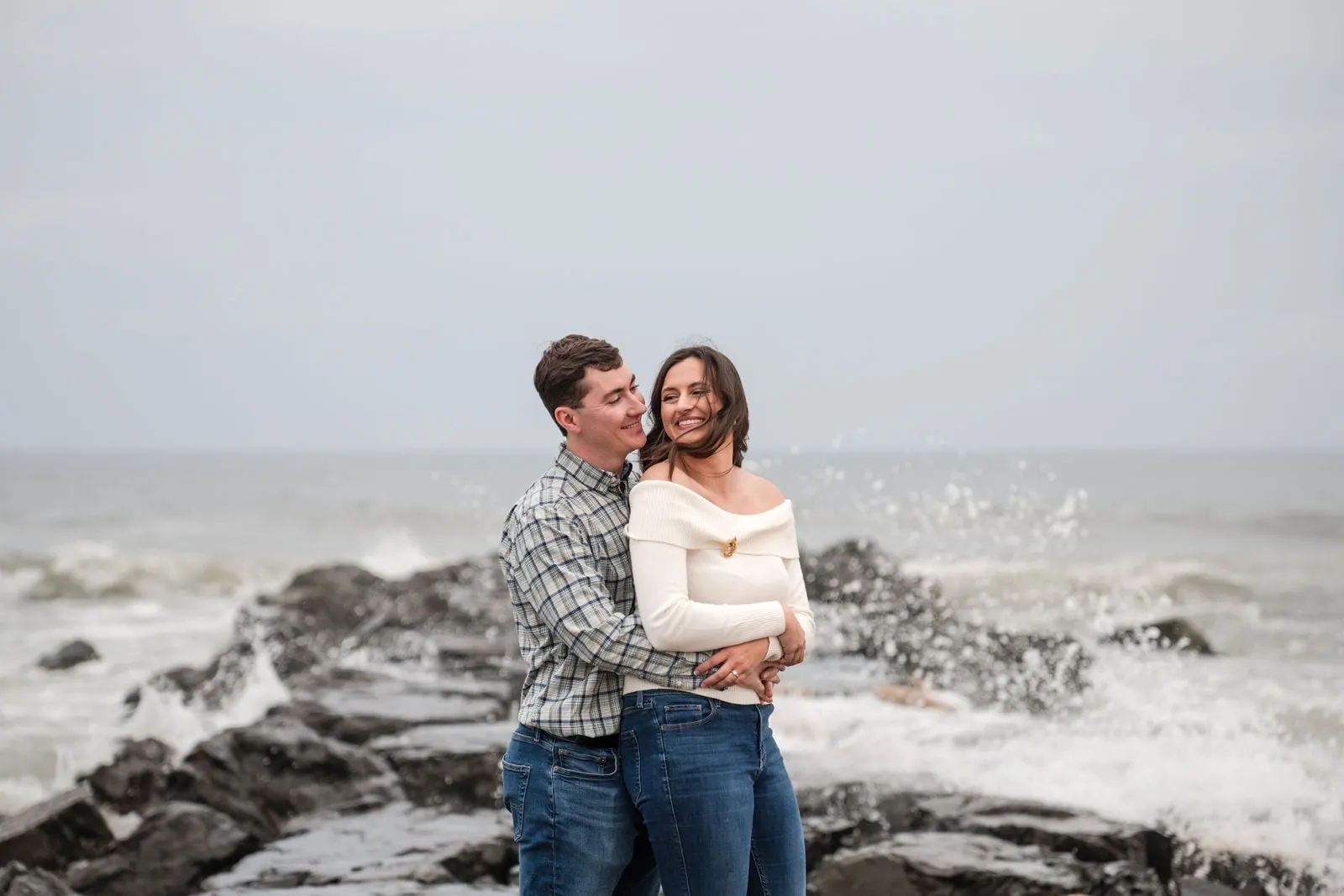 Couple embracing on the jetty as a wave splashes behind them