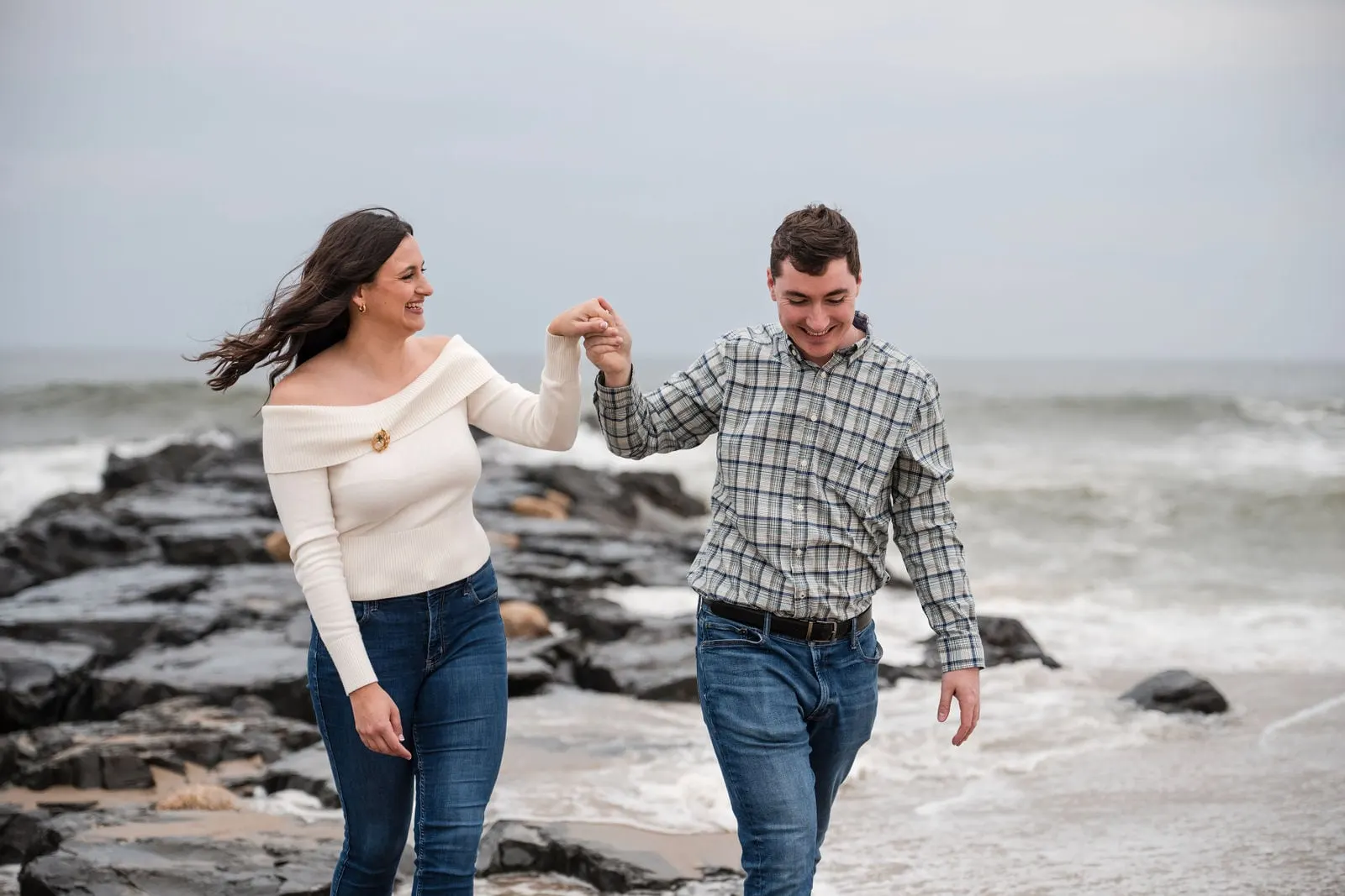 Fiancé helping his partner down from the rock jetty, both laughing
