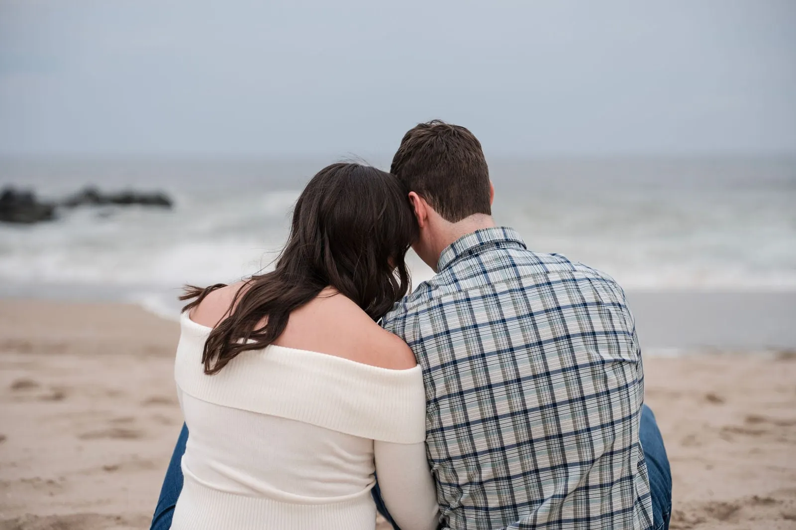Couple sitting close together facing the ocean