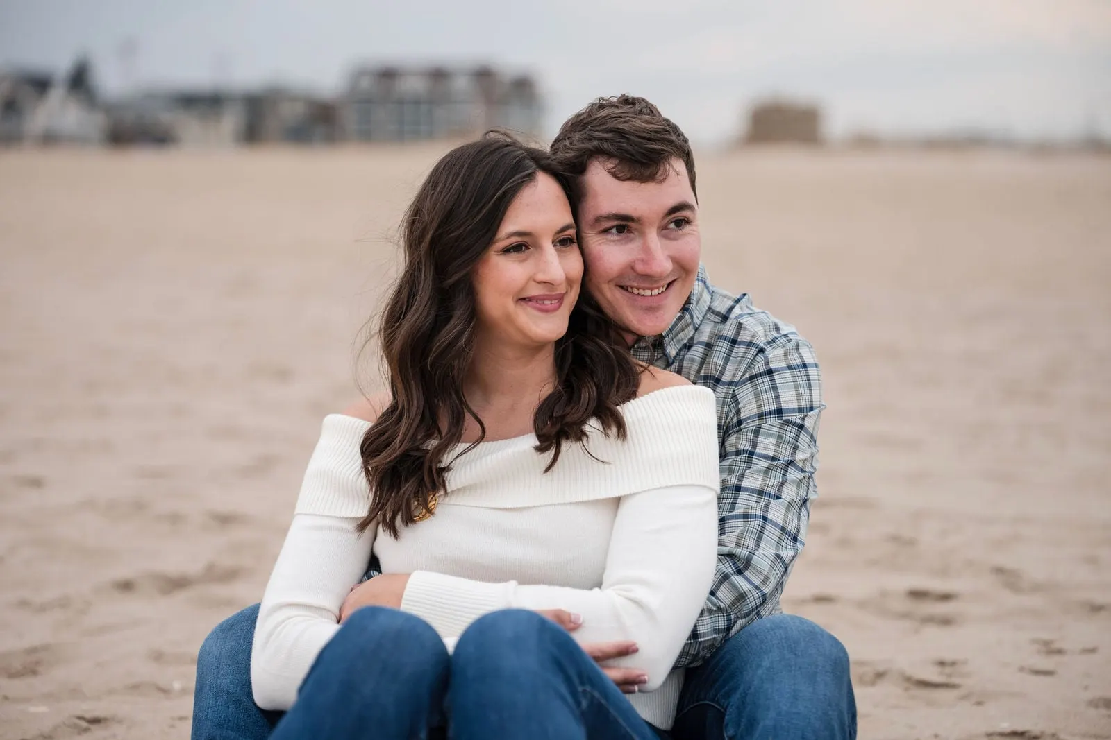 Engaged couple smiling while sitting on the sand