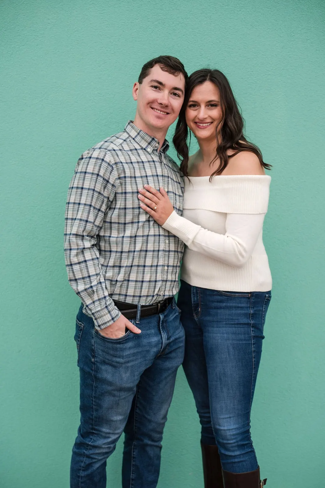 Engaged couple smiling in front of a turquoise wall in Asbury Park, New Jersey