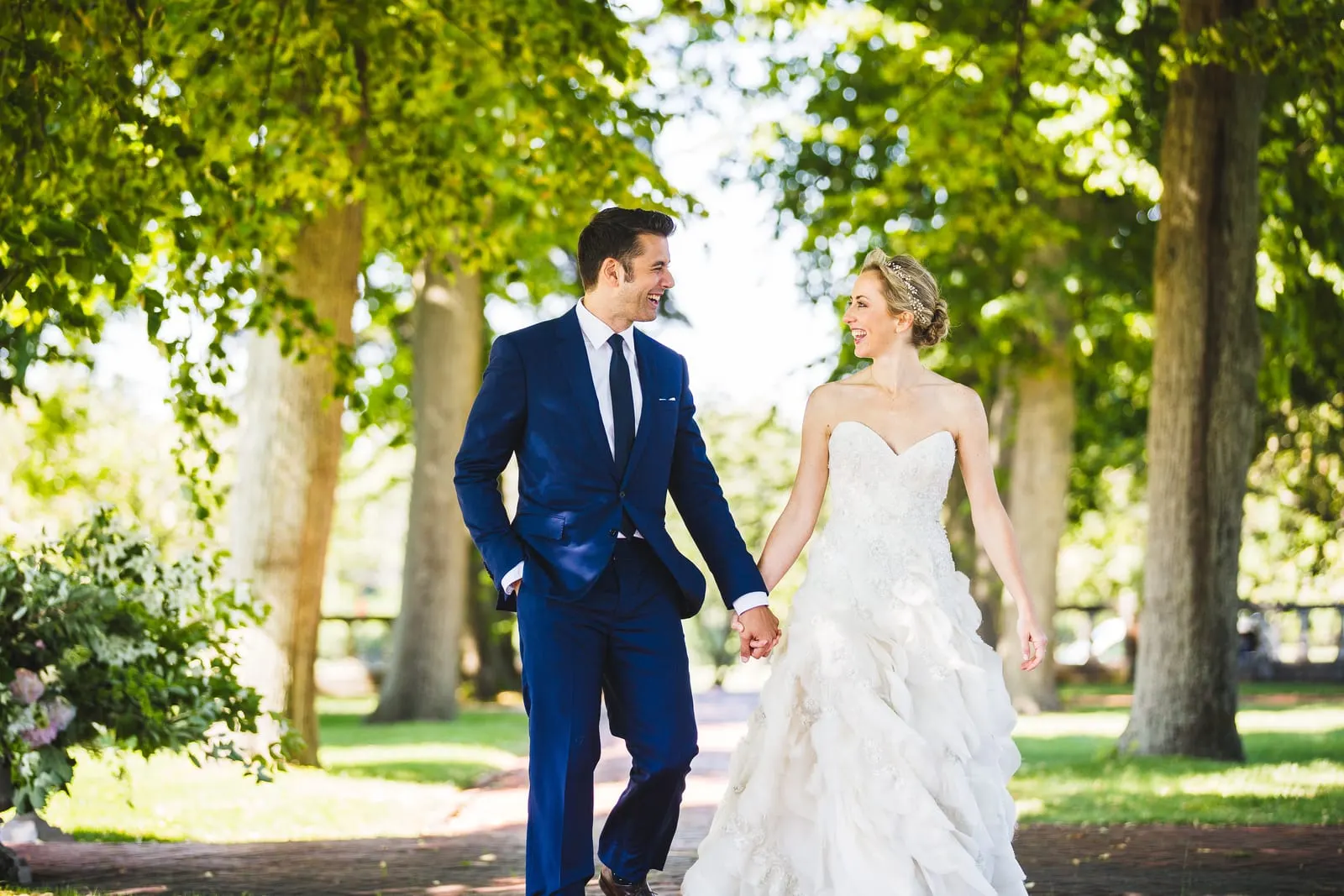 Bride and groom walking hand in hand along a tree-lined path