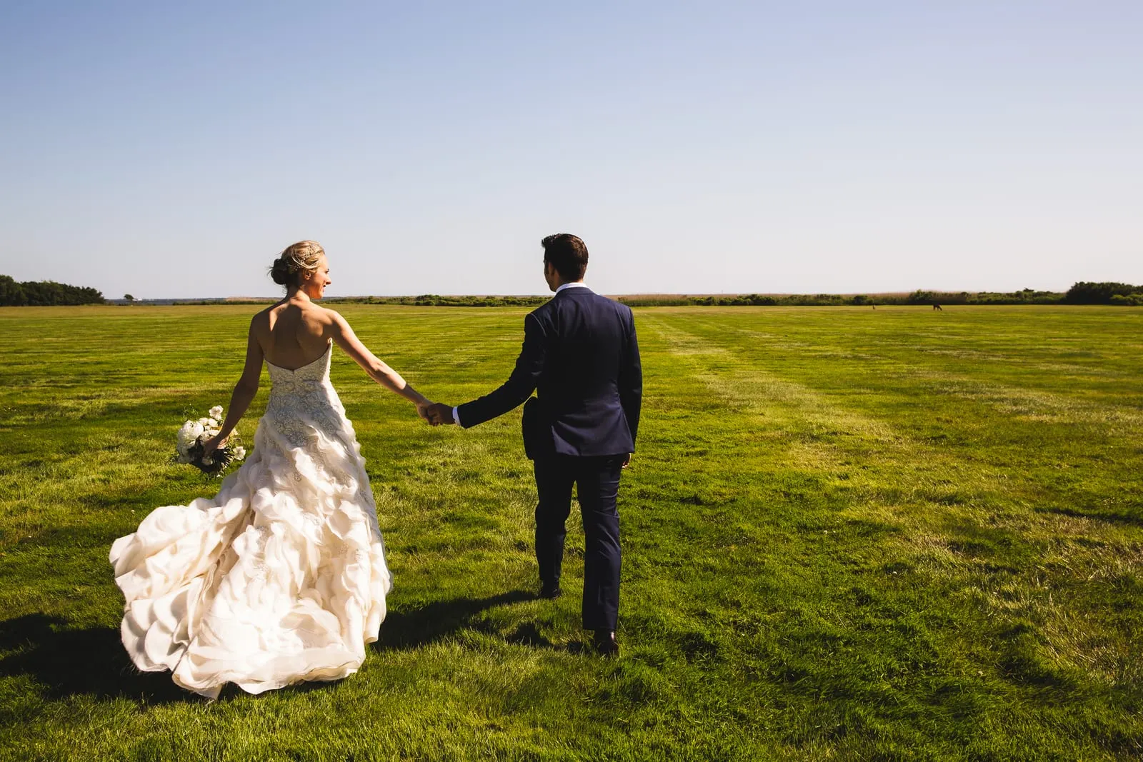 Bride and groom walking hand in hand across the open lawn
