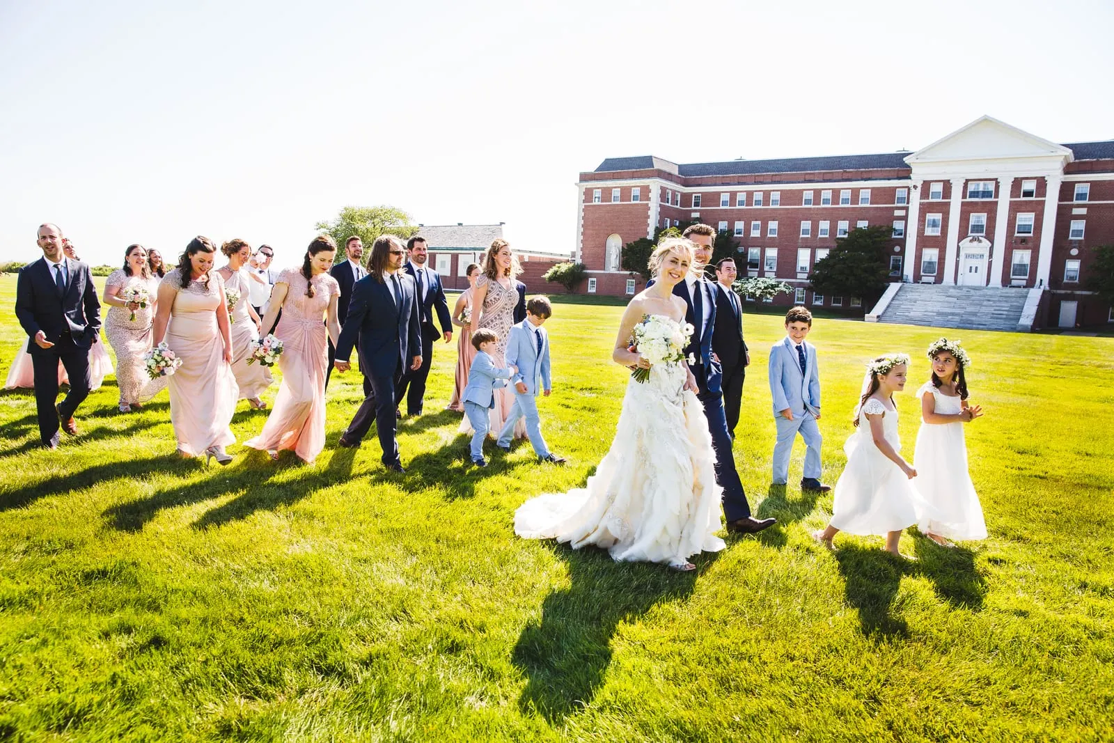 Wedding party walking across the lawn with Bourne Mansion behind them