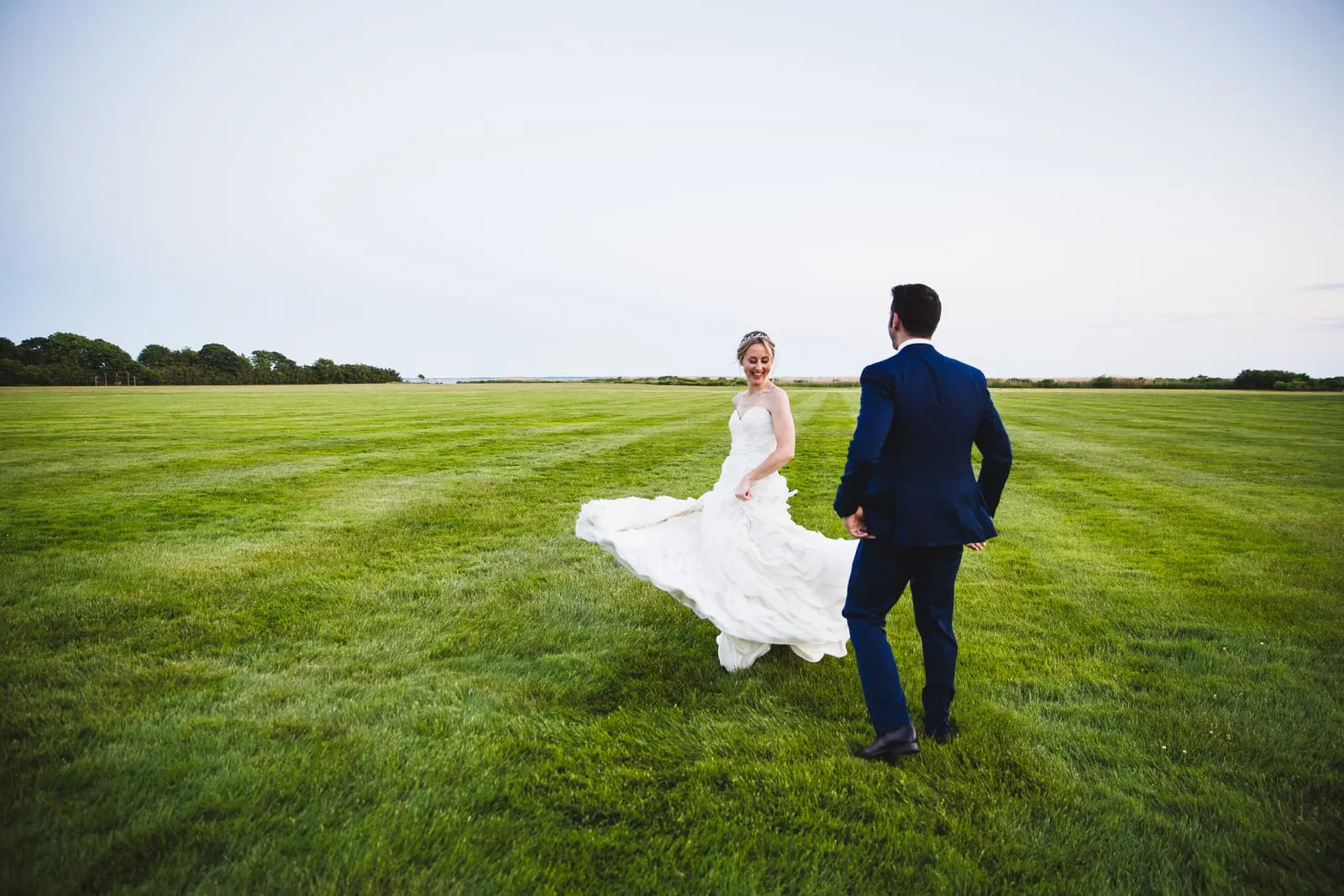 Bride's gown flowing as the couple walks across the lawn at sunset