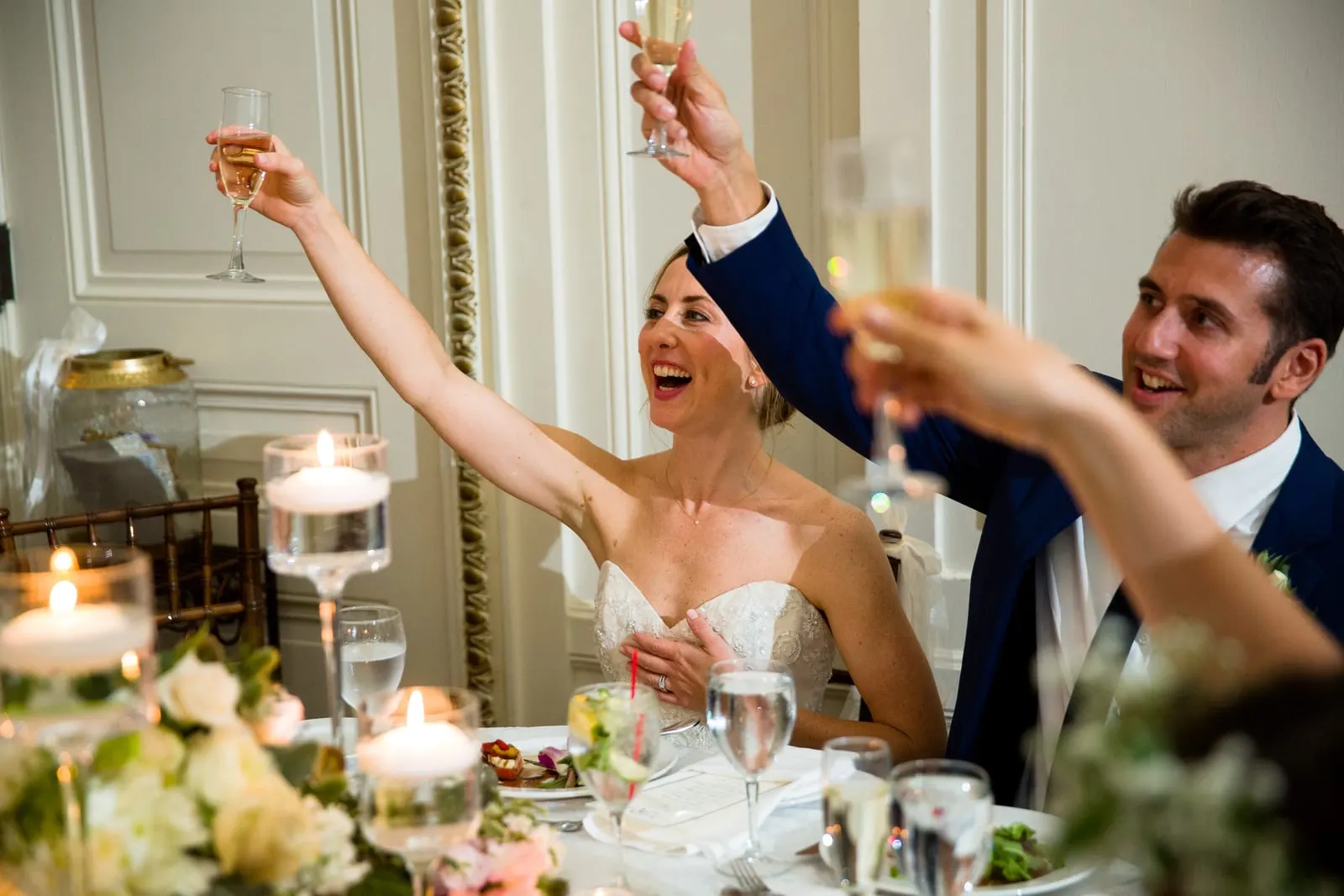 Bride raising her arms in celebration at the sweetheart table
