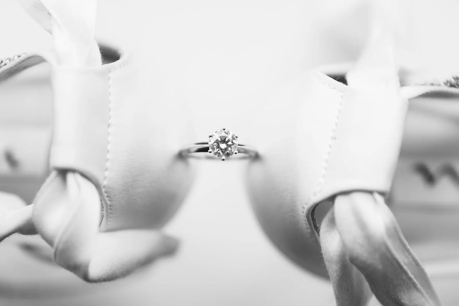 Engagement ring resting between the bride's satin heels, in black and white
