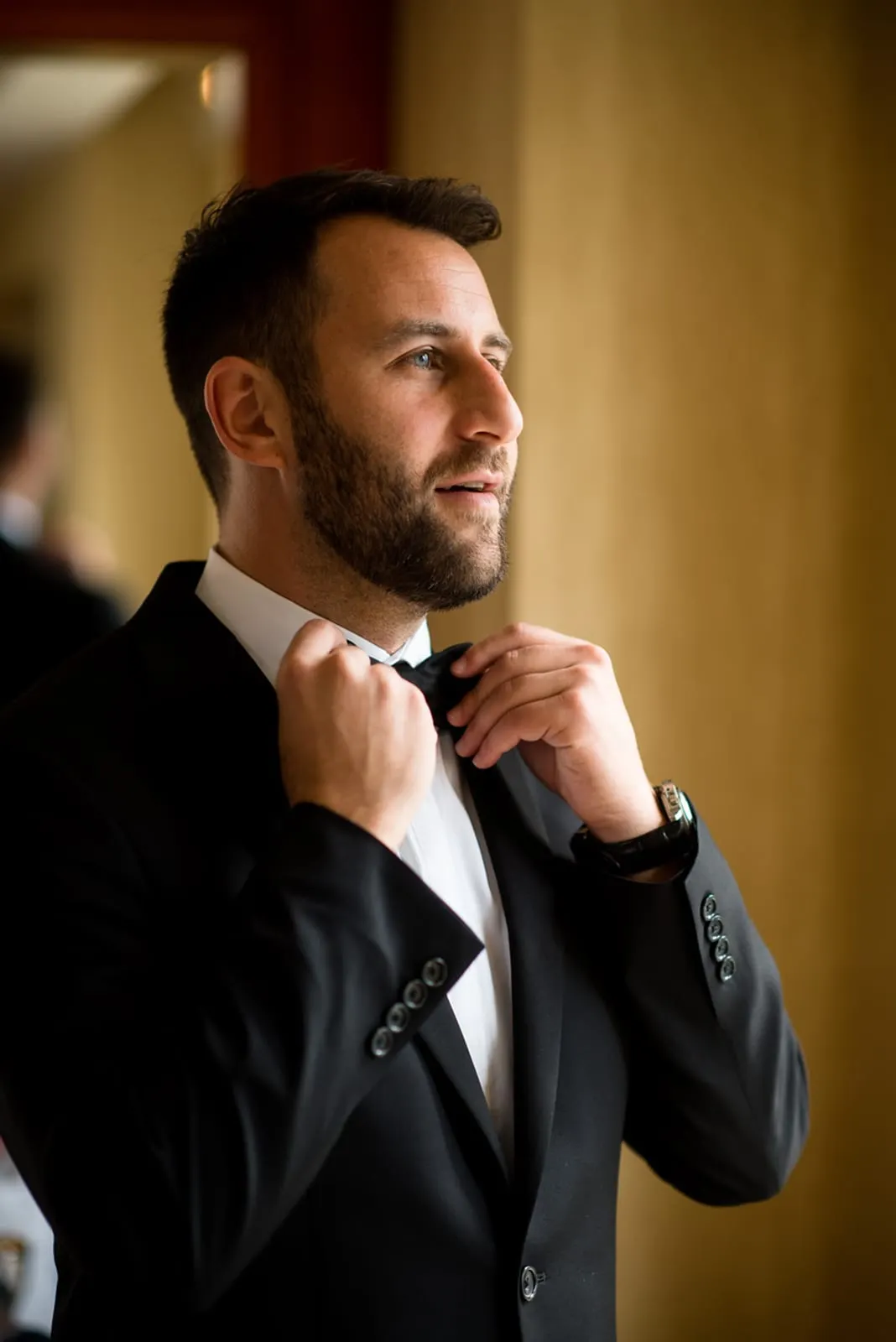 Groom adjusting his bow tie by the window