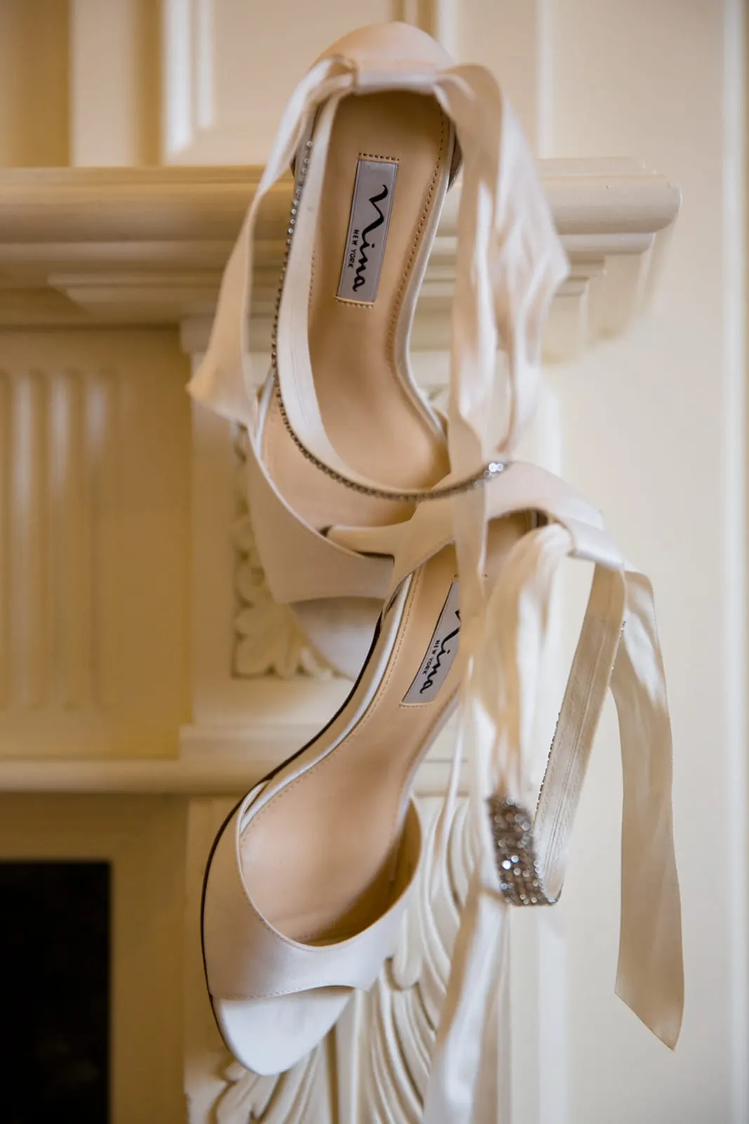 Satin bridal sandals hanging from a carved fireplace mantel