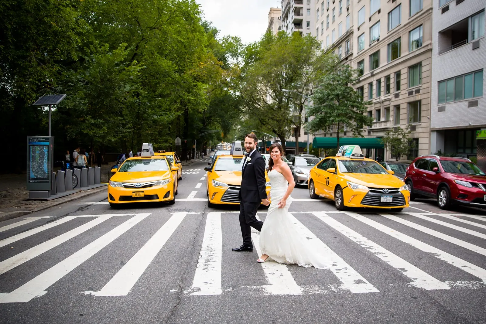 Bride and groom in a crosswalk with yellow taxis on Central Park South