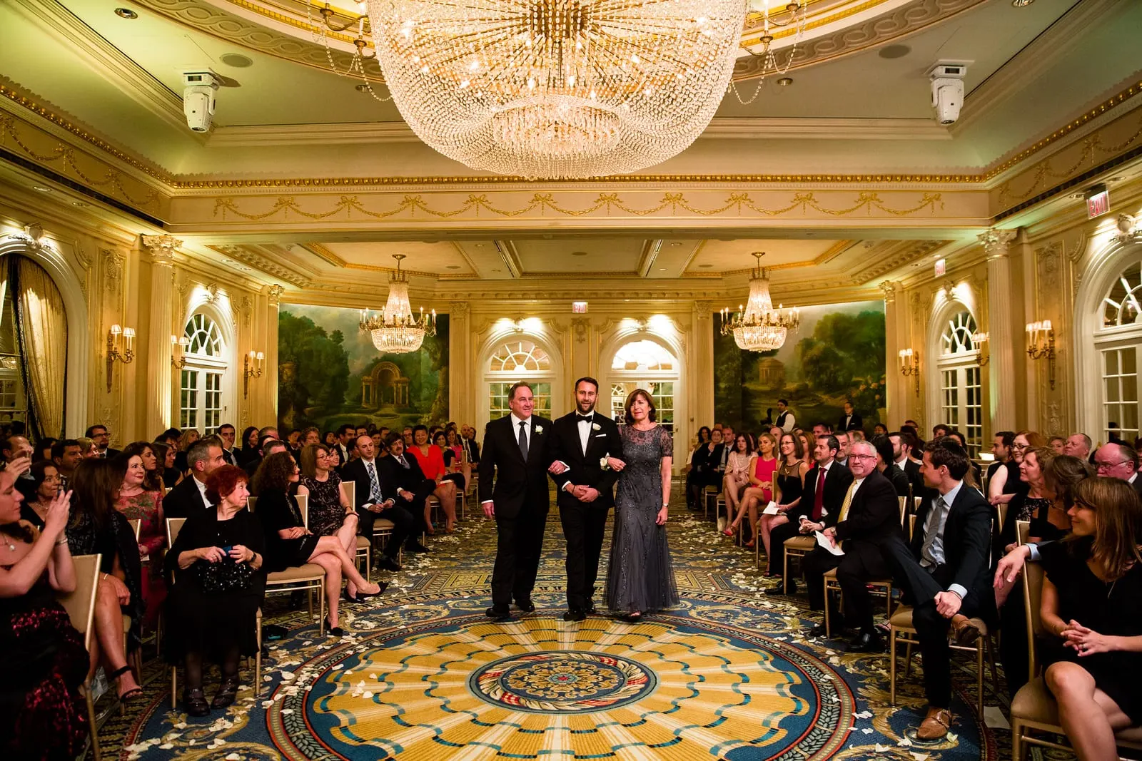 Groom walking down the aisle with his parents in the Essex House ballroom