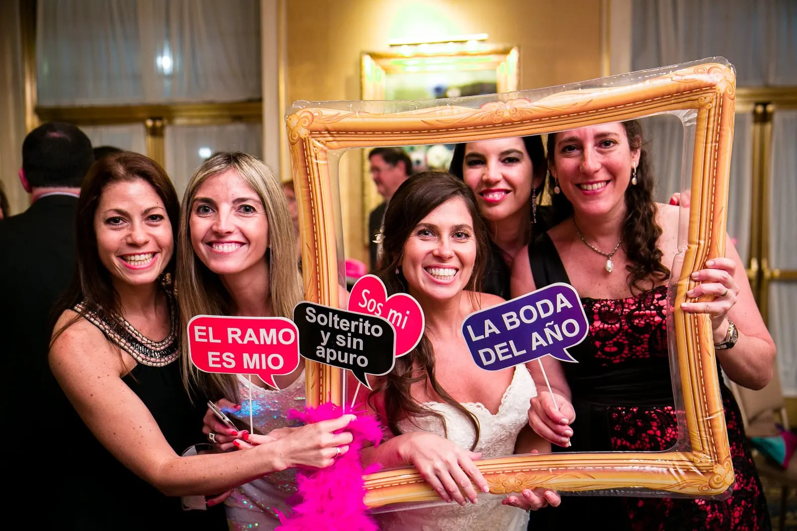 Bride and friends posing with a gold frame and signs during cocktail hour