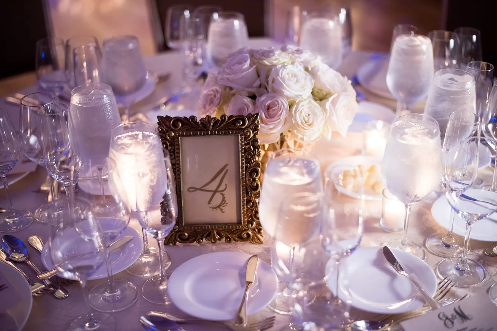 Gold-framed table number and white roses on a reception table