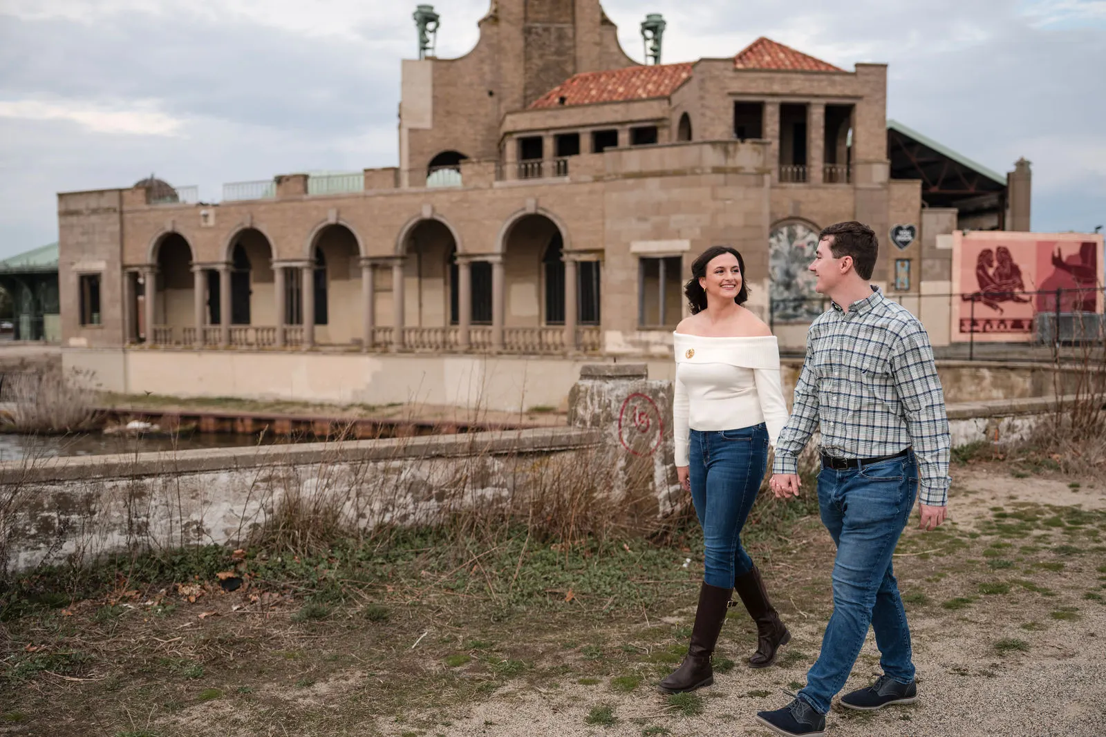 Engaged couple walking in front of the historic steam plant building near the boardwalk in Asbury Park, New Jersey