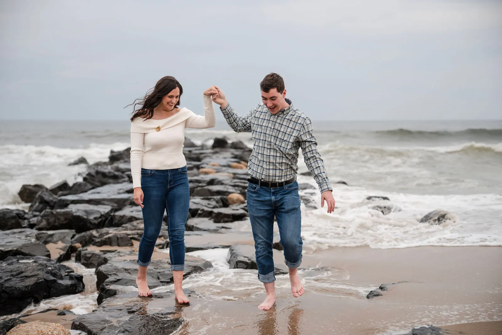 Barefoot couple holding hands and stepping off a rock jetty as waves wash in at Asbury Park, NJ
