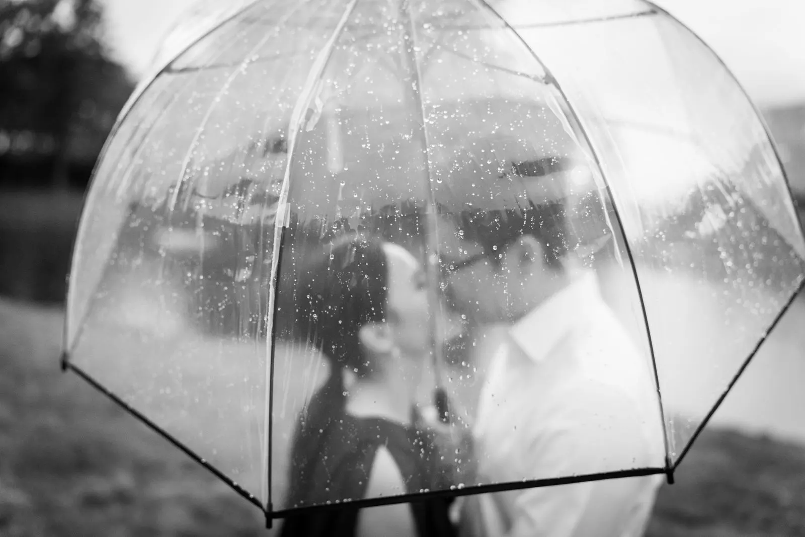 Black and white photo of an engaged couple kissing behind a rain-covered clear umbrella in Holmdel, New Jersey