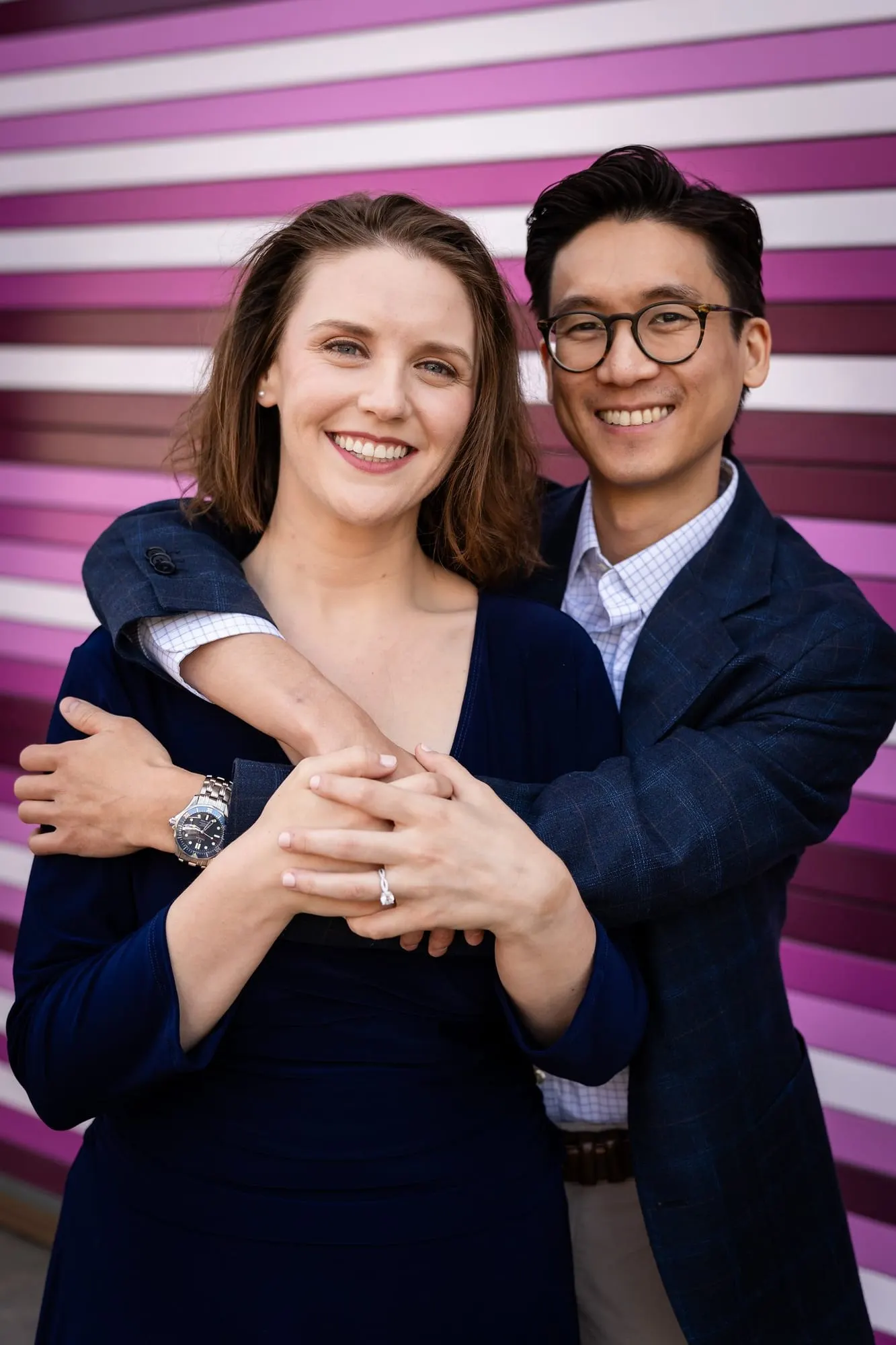 Engaged couple embracing in front of a purple and white striped wall in Long Island City