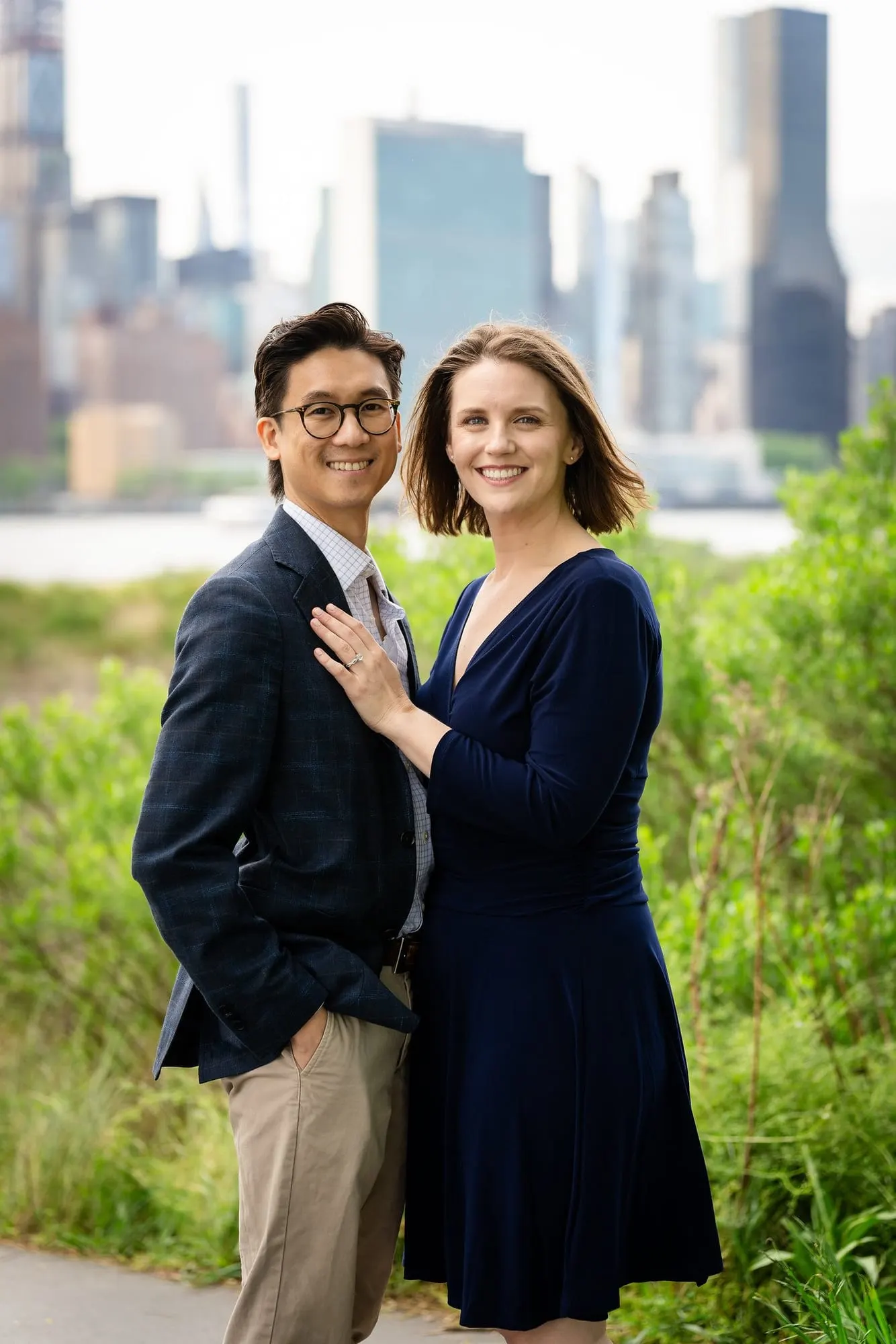 Couple standing among tall grasses with Midtown Manhattan towers behind them