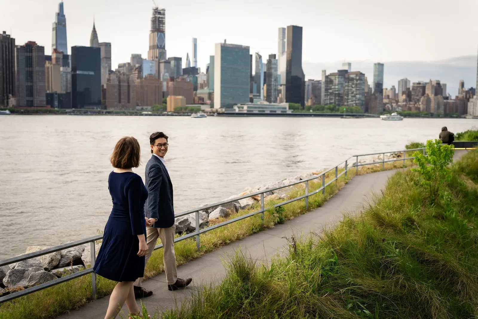Couple walking along a waterfront path with the Manhattan skyline across the river