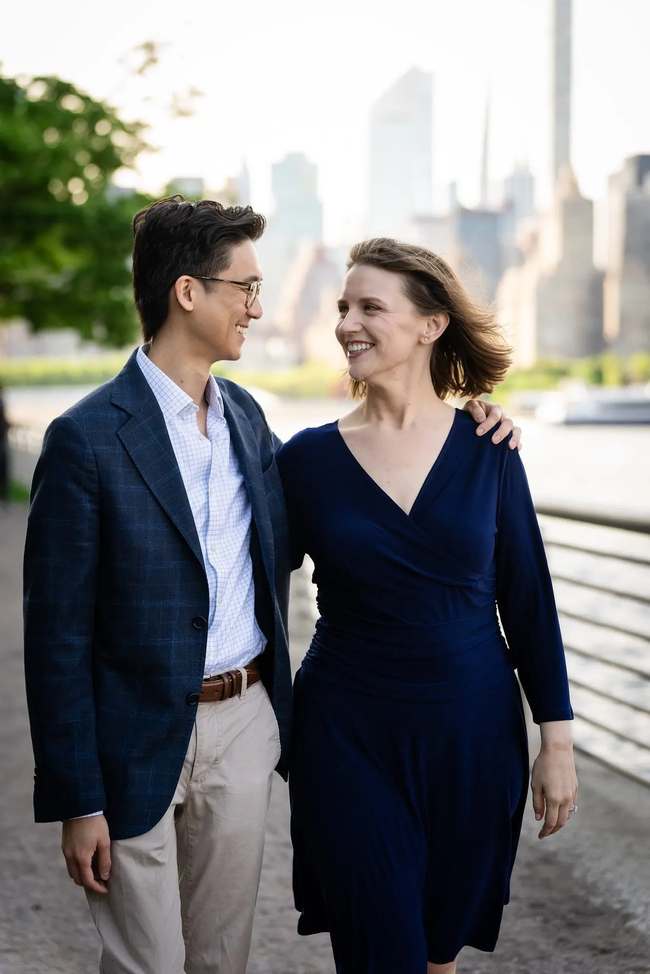 Couple walking arm in arm with the Manhattan skyline behind them at Gantry Plaza State Park