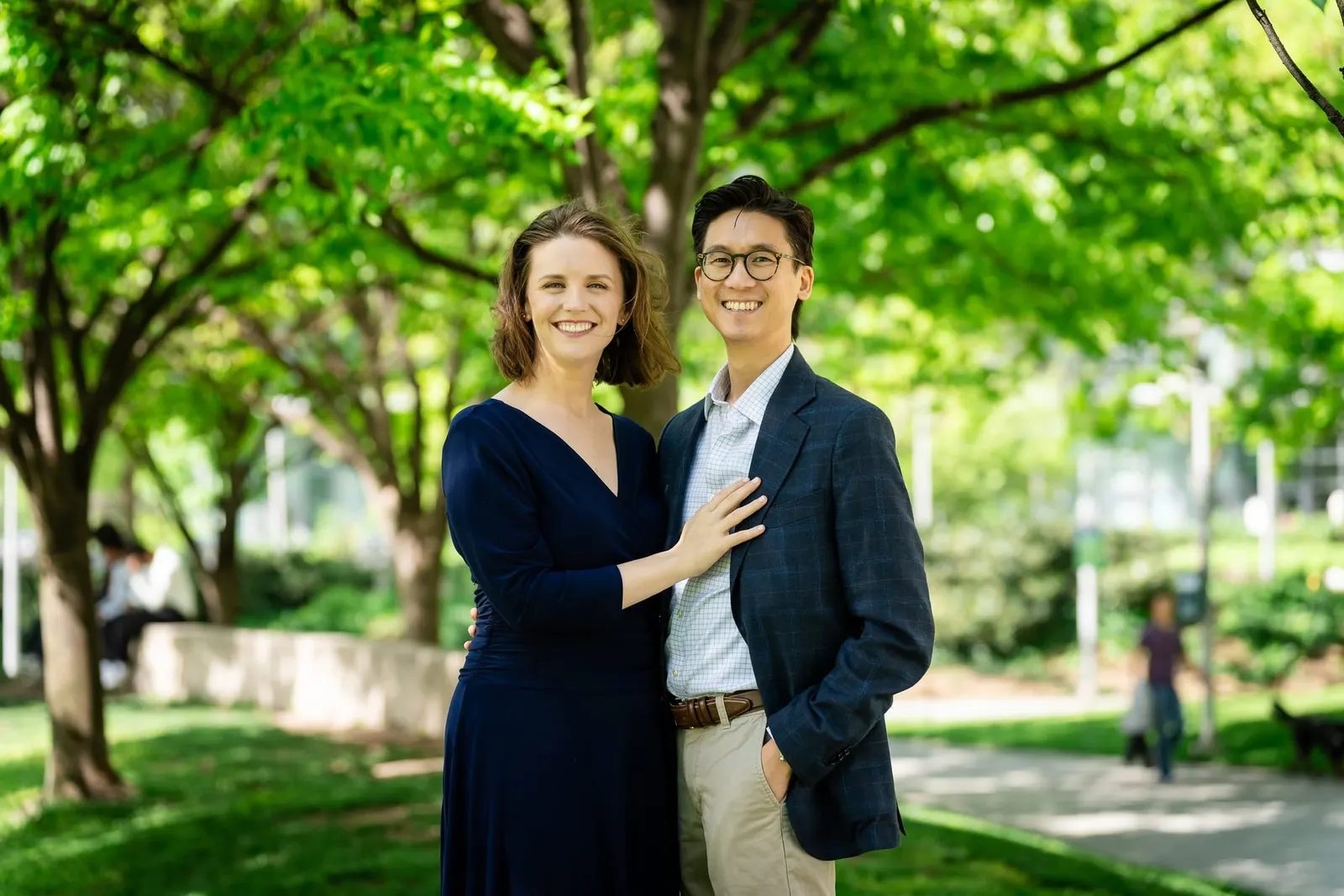Engaged couple standing together under leafy trees at Gantry Plaza State Park
