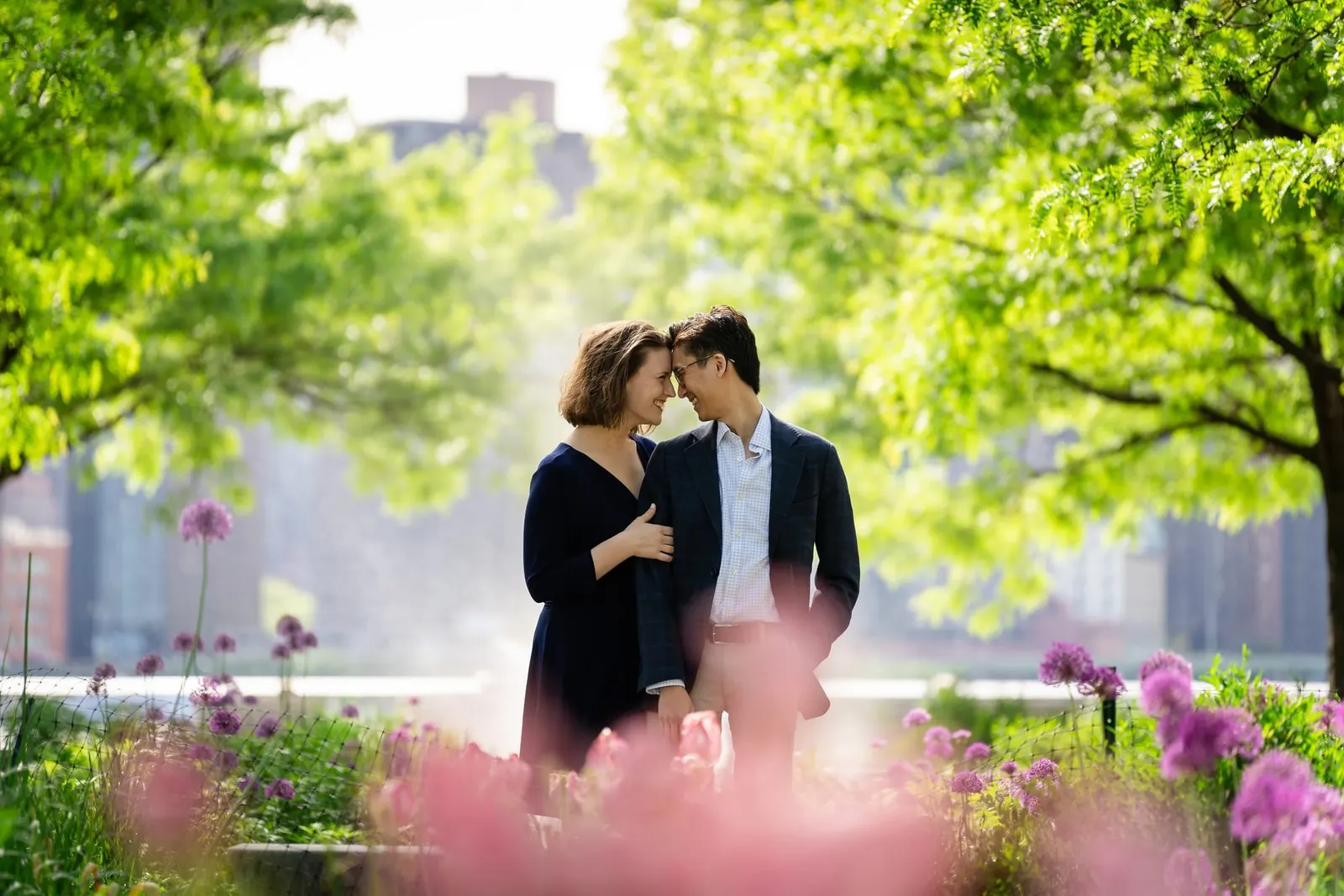 Couple touching foreheads among pink flowers with the Midtown skyline behind them
