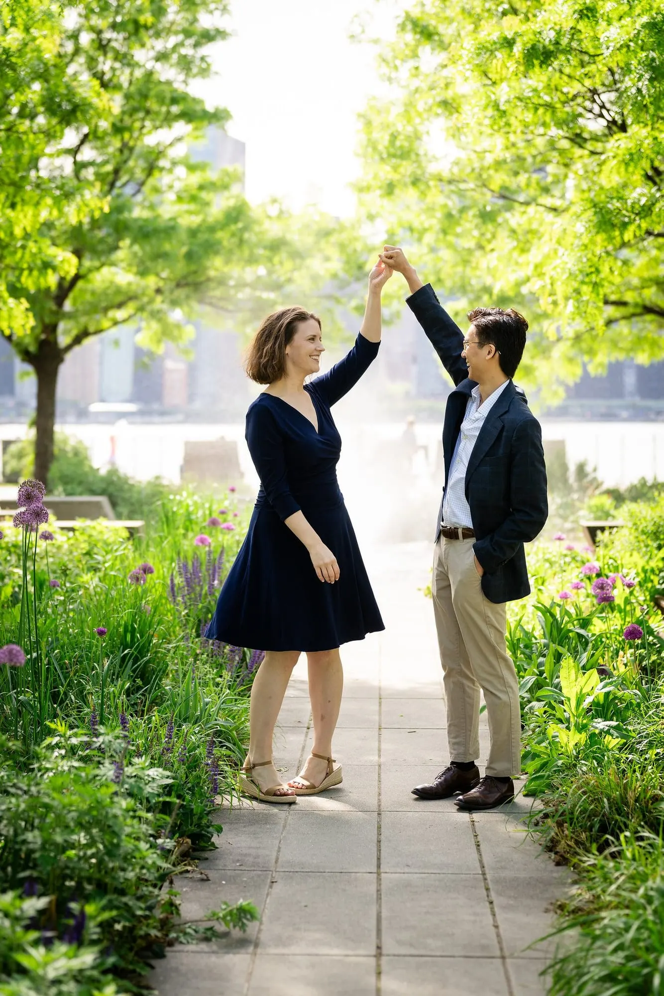 Man twirling his fiancée on a garden path in Long Island City