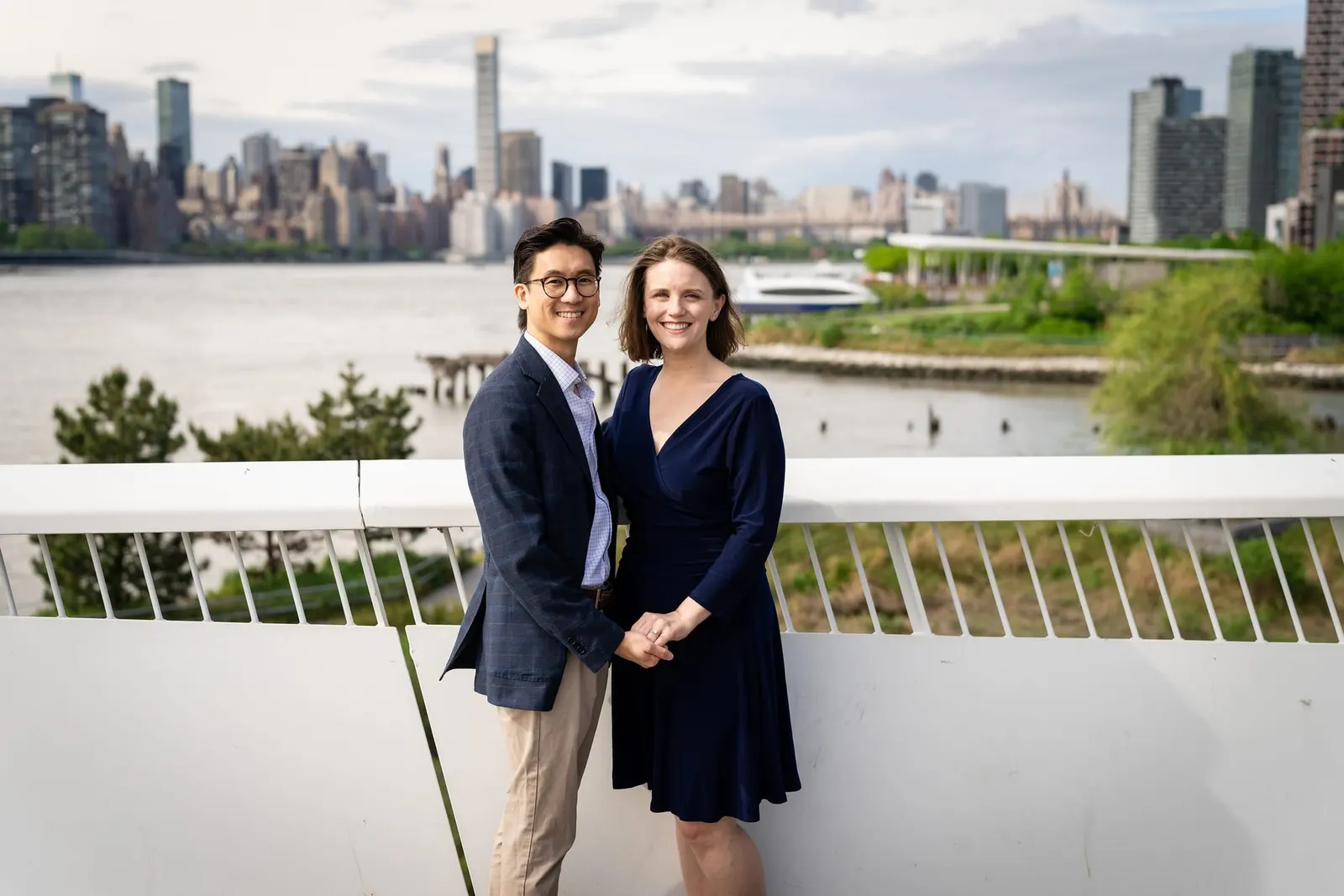 Couple at the waterfront railing with the Manhattan skyline across the East River