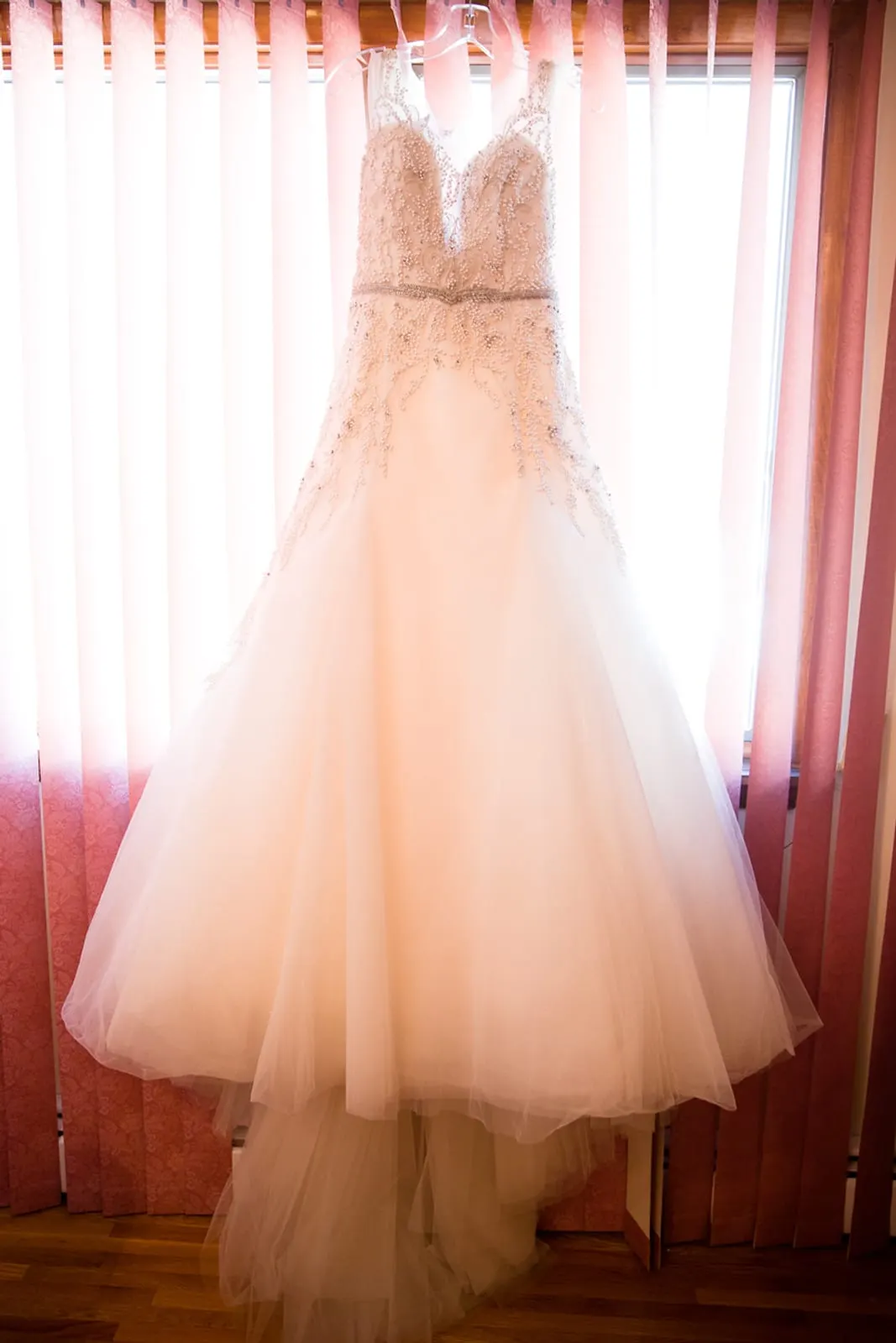 Beaded ballgown hanging in a sunlit window on the wedding morning