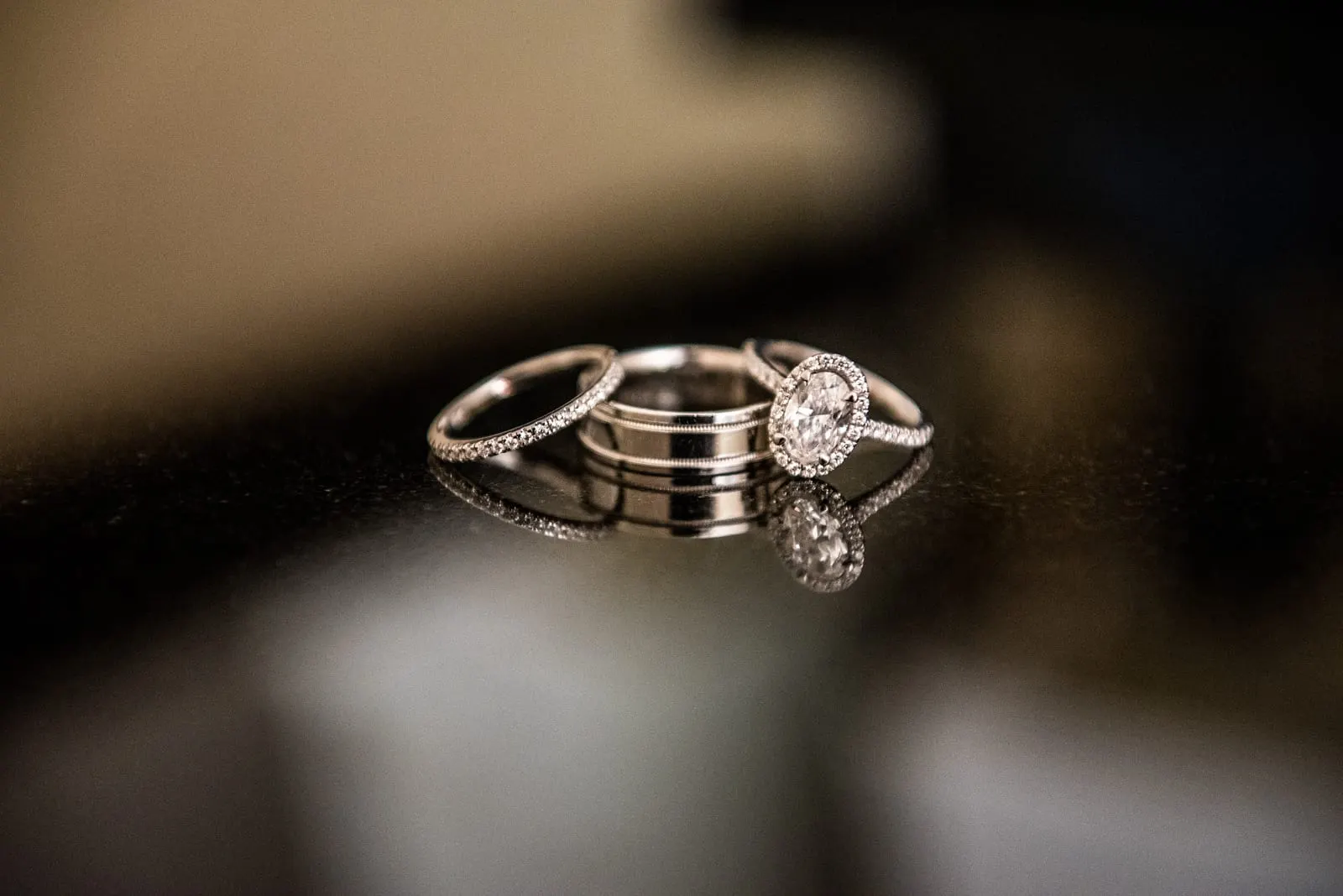 Engagement ring and wedding bands reflected on a dark table