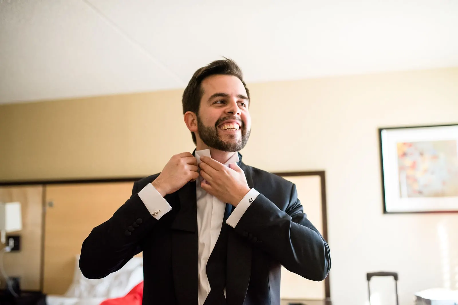 Groom smiling as he straightens his bow tie
