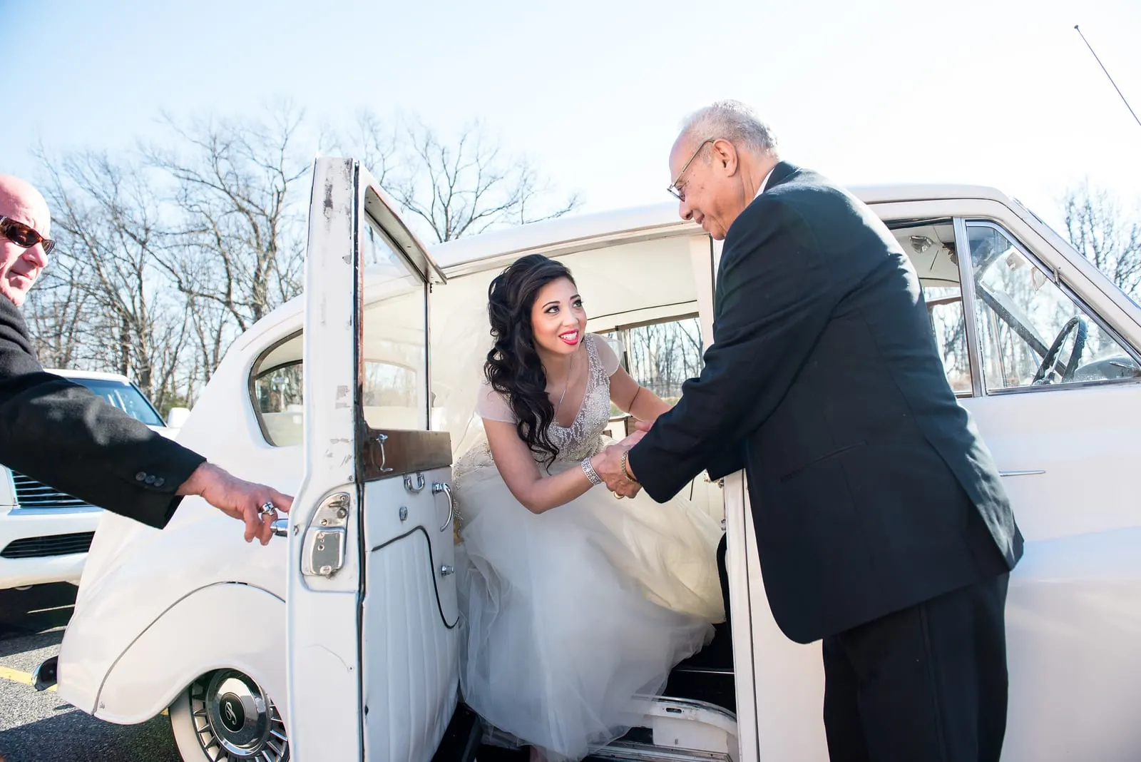 Bride's father helping her out of a vintage white car at the cathedral